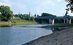 A middle-sized river with sandy and grassy banks flows under a bridge.