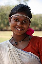 A dark-skinned woman with a bindi, tilting her head and smiling at the camera