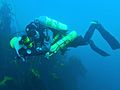 A diver is carrying two cylinders, one on his back and the other at his side. 