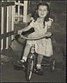 Girl with ringlets and a white dress riding a delta tricycle.