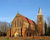 A Gothic Revival church in red brick with stone bands and an almost separate south tower surmounted by a lead-covered spire