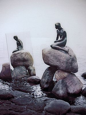 A statue of a mermaid sitting on a rock, surrounded by water.