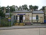 A beige-bricked building with a rectangular, dark blue sign reading "MILL HILL STATION" in white letters all under a blue sky with white clouds