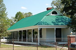 White building with wrap-around porch and green roof.