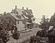 Sepia-toned 1890s photo of dirt road with Queen Anne-style apartment at the end, with water in the distance