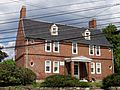 A 2+ story brick colonial house. The windows are comparatively narrow, and there are small round windows near the corners of.