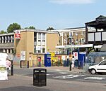 A beige building with a rectangular, white sign reading "Welcome to Kensington Olympia" in dark blue letters all under a light blue sky