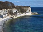 White cliffs topped with sparse grass partially encircle the blue ocean