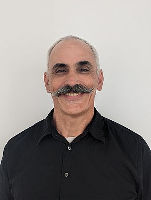 Evan Prodromou smiling and facing the camera with his back against a white background