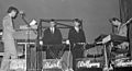 A black and white photograph of four members of Kraftwerk onstage, each with a synthesizer