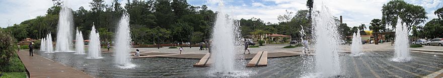 A fountain in a square with at least 10 jets of water and people walking around it