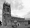 A church seen from the southwest with the tower on the left and the body of the church, with clerestory and south aisle, to the right. The tower has crocketted pinnacles and the body of the church is crenellated