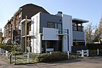 Modern house of white and grey flat, angular concrete surfaces. The modern house is attached to several older, traditional houses.