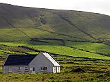 New-looking grey house in front of a high green hillside, which is lined with dark hedgerows.