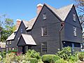 A large many-gabled brown house with a flower garden in front.