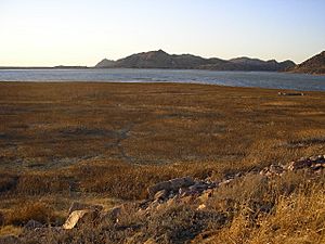 A photo of a dry lakebed with some ruined foundations