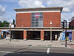 A red-bricked building with a rectangular, grey sign reading "SUDBURY HILL STATION" in black letters all und er a blue sky with white clouds