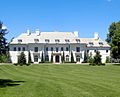 White mansion with four chimneys, trees lining the front, and many windows