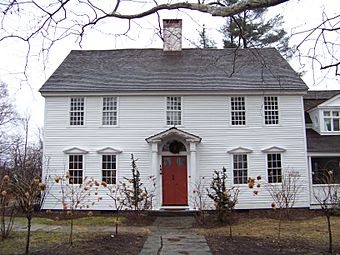 A white wooden house with no shutters, roof, and central chimney, and trees around