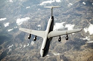 Top view of four-engine jet transport in-flight above mountain range.