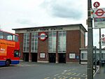 A red-bricked building with a rectangular, grey sign reading "SUDBURY TOWN STATION" in black letters all under a blue sky