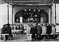 Soldiers and other sitting on benches in front of a stage