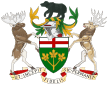 A central shield with the upper part showing the red cross of St. George and the lower part showing three golden maple leaves on a green background. There is a black bear on top of a knight's helmet above the shield with a moose to the left and a Canadian deer to the right. The province's motto "Ut incepit Fidelis sic permanet", Latin for "Loyal she began, loyal she remains" is written below the crest.