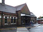 A brown-bricked building with a rectangular, dark blue sign reading "RUISLIP STATION" in white letters all under a clear, white sky