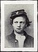 Head and shoulders of a young white man with unkempt hair sticking out from under a tilted forage cap. He is wearing an open jacket over a white shirt.