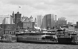 The Whitehall Terminal, a ferry terminal, is in the foreground between skyscrapers behind it and a harbor in front of it.