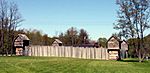 A wooden stockade fort with a green lawn in the foreground.