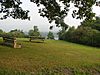 A bench and a picnic table on a grassy slope with a lake visible through trees in the distance