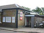 A small, brown-bricked building with a brown-shingled roof and a silver, two-wheeled vehicle sitting idle in front all under a white sky