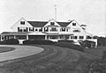 A large white house with three large gables and a porch running for much of its width stands before an expansive lawn and curved drive.