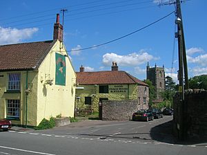 Yellow painted building fronting the road is nearest the camera. In the background is the square stone tower.