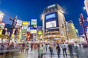 People cross busy Shibuya intersection lined with electronic billboards at dusk