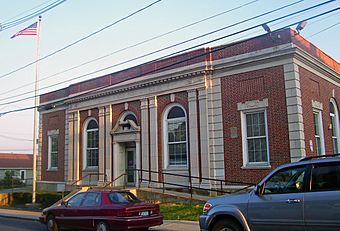 Front view of the Haverstraw post office, showing extensive architectural ornamentation, in evening sunlight with two cars parked in front