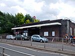 A brown-bricked building with a rectangular, dark blue sign reading "UPNEY STATION" in white letters all under a light blue sky with white clouds