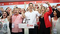 Pedro Sánchez wearing a white shirt and cheering with multiple people