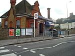 A brown-and-red bricked building with a rectangular, dark blue sign reading "WIMBLEDON PARK STATION" in white letters all under a blue sky