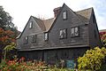 A brown-painted colonial house with two large front-facing gable dormers. The windows have very small diamond panes of glass.