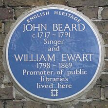 A Blue plaque on a brick wall with the words "John Beard C1717 – 1791 Singer and William Ewart 1798 – 1861 Promoter of Public Libraries