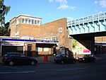 A brown-bricked building with a rectangular, dark blue sign reading "RUISLIP MANOR STATION" in white letters all under a light blue sky