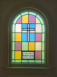 a colorfull glass window with a subdued cross in it and the text "in loving memory Rev. William T. Collins Jan. 1901-Apr. 1951"