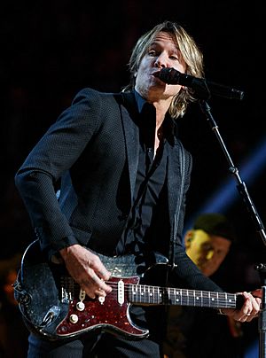 Keith Urban, singing into a microphone while playing an electric guitar