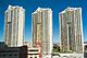 Distant ground-level view of three identical 38-story towers; the building has gold colored windows and balconies on each floor.