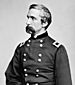 Profile of a white man with a drooping mustache wearing a double-breasted military jacket with a rectangular patch and star on each shoulder.