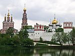 A walled monastery with red and white towers with golden domes