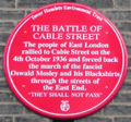 Red plaque from Tower Hamlets Environment Trust reading The Battle of Cable Street. The people of East London rallied to Cable Street on the 4th October 1936 and forced back the march of the fascist Oswald Mosley and his Blackshirts through the streets of the East End. 'They Shall Not Pass'