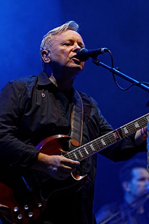 Sumner playing a guitar and singing into a microphone onstage